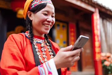 A cheerful woman in traditional clothing using her smartphone during a festive moment, showing how easily the DBJL app fits into everyday life.